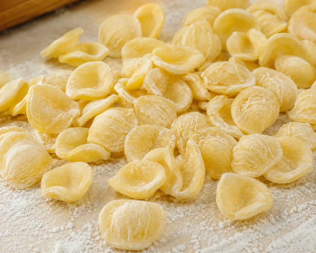 Pâtes orechiette fraîches sur plan de travail fariné, texture délicate et pâtes prêtes à cuisiner.