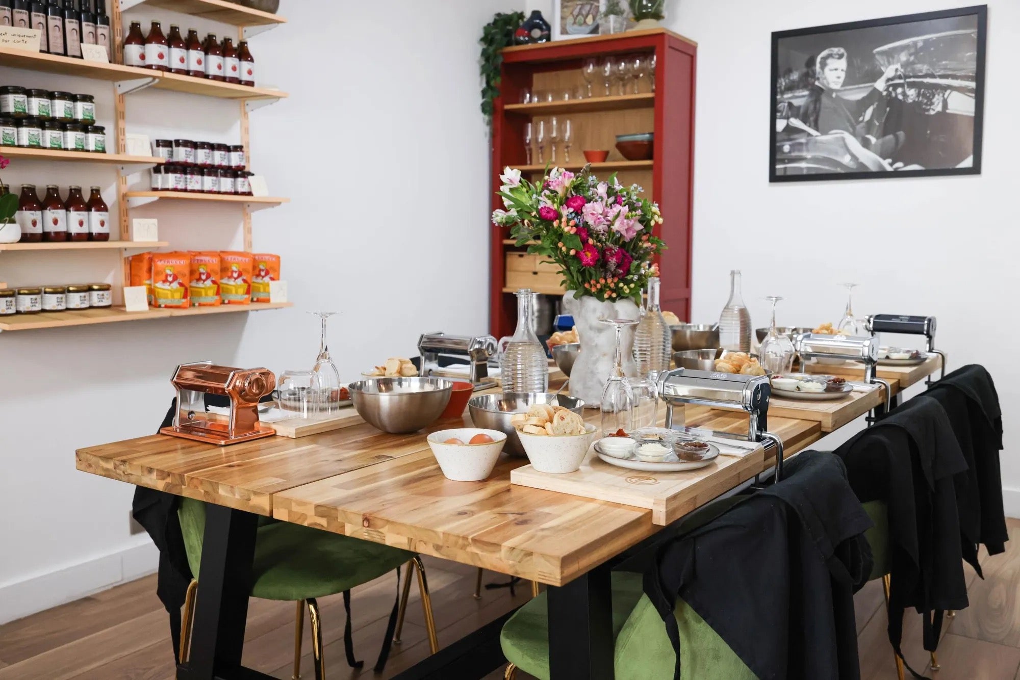 Table conviviale en atelier avec appareil à pâtes, bols et couverts, vase de fleurs et boissons, ambiance chaleureuse.
