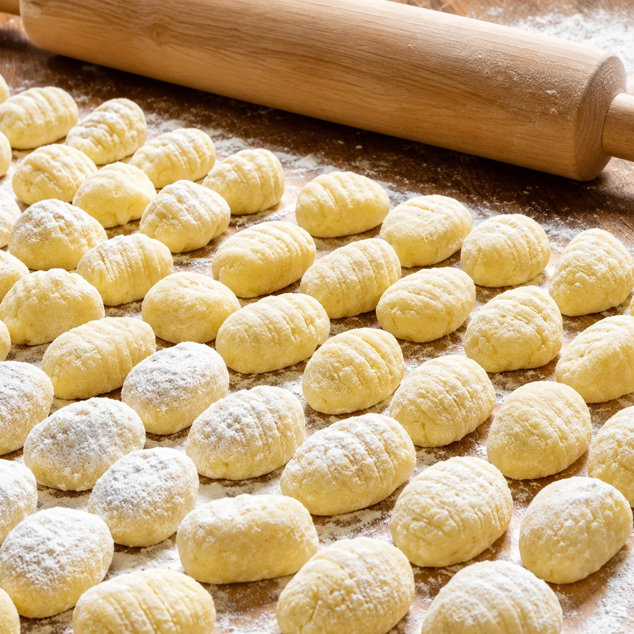 Gnocchis frais en préparation sur plan de travail fariné avec planche en bois et morceaux en pâte farcie.
